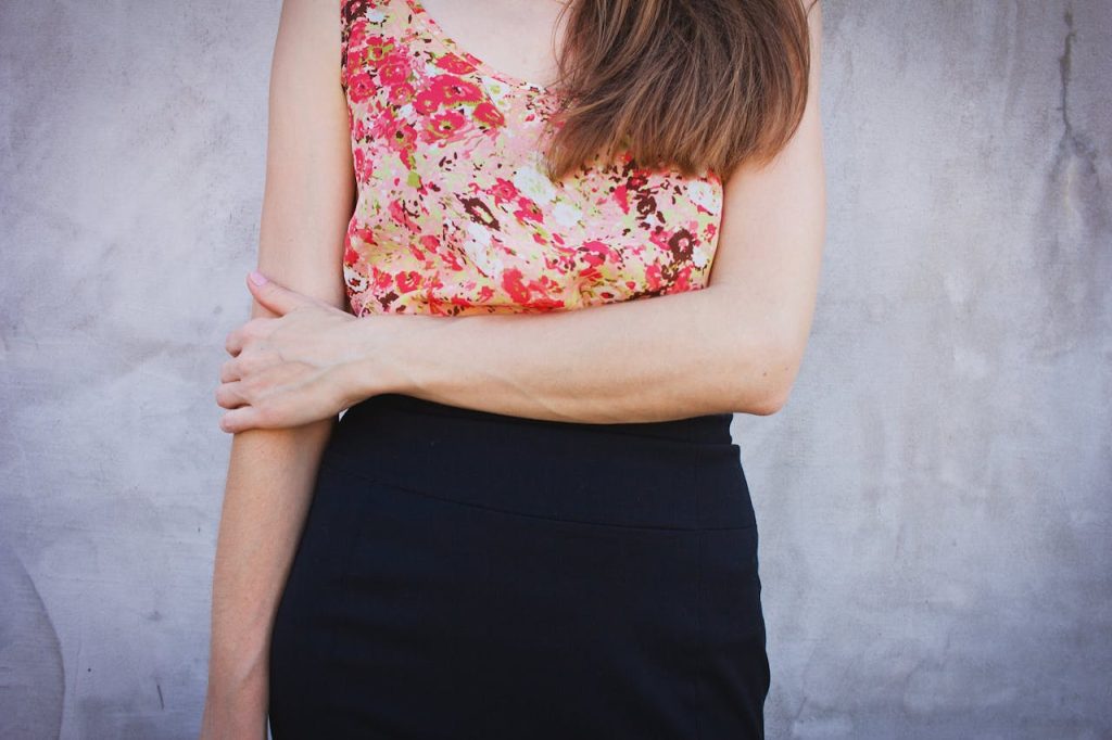 Close-up of a woman wearing a floral top and black skirt, standing against a concrete wall.